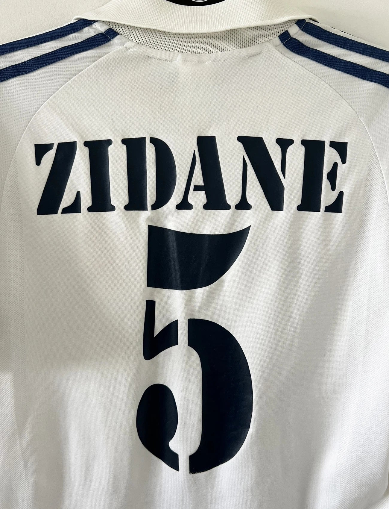 Maillot de foot vintage domicile du real madrid de la saison 2001-2002. Le maillot est de couleur blanc et noir. On peut retrouver l'équipementier adidas et le sponsor Real Madrid.com. Le maillot est floqué du numéro 5 Zinedine Zidane. Il s'agit d'un maillot authentique