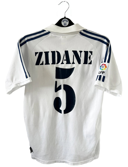Maillot de foot vintage domicile du real madrid de la saison 2001-2002. Le maillot est de couleur blanc et noir. On peut retrouver l'équipementier adidas et le sponsor Real Madrid.com. Le maillot est floqué du numéro 5 Zinedine Zidane. Il s'agit d'un maillot authentique