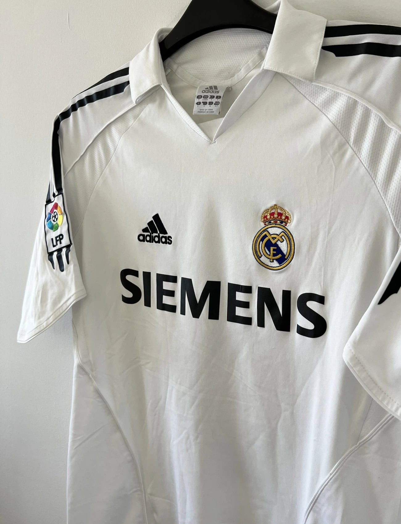 Maillot de foot vintage domicile du Real Madrid de la saison 2005/2006. Le maillot est de couleur blanc et noir. On peut retrouver l'équipementier adidas et le sponsor siemens. Le maillot est floqué du numéro 5 Zinedine Zidane. Le maillot possède l'étiquette d'authenticité avec les numéros 109879. Il s'agit d'un maillot authentique d'époque.