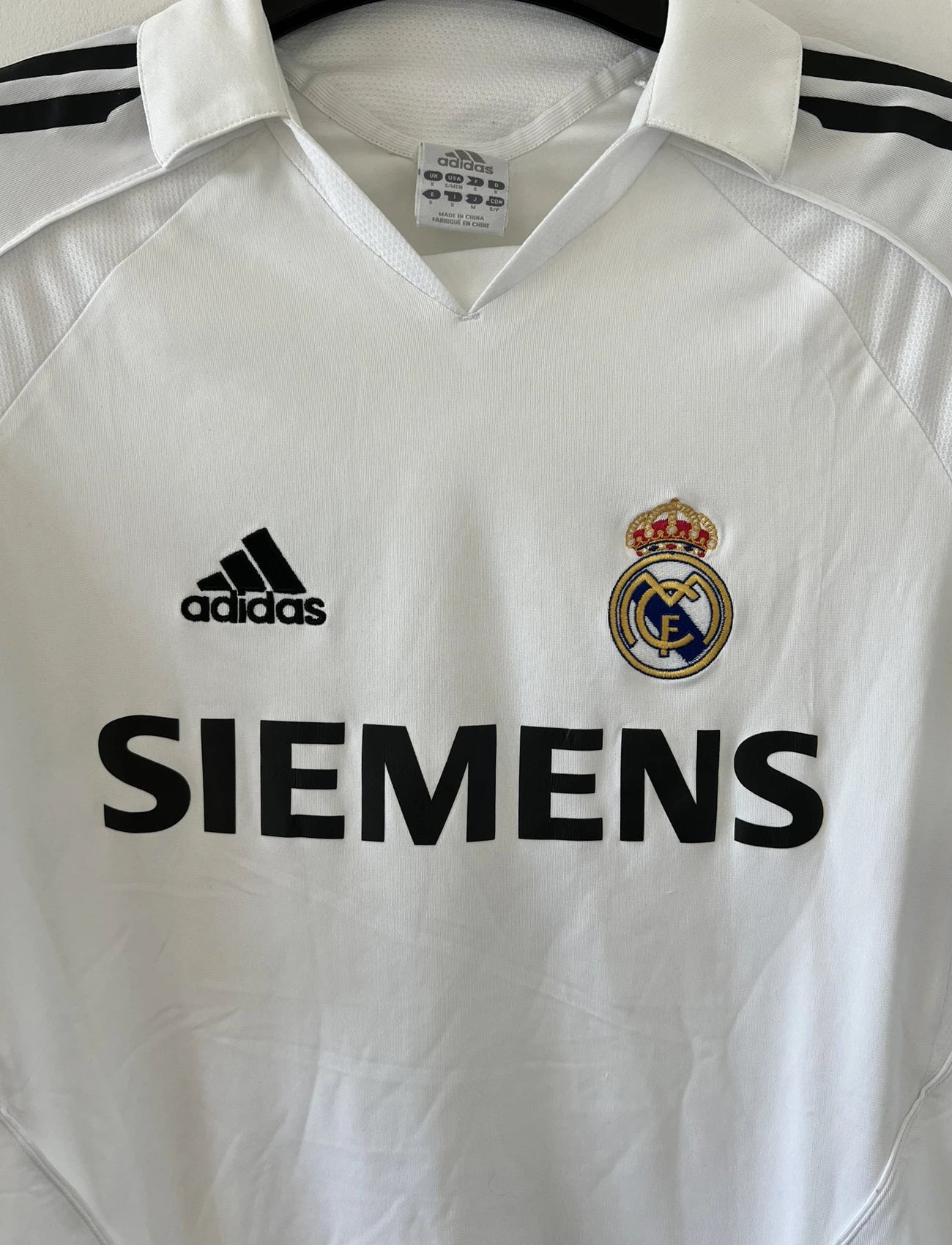 Maillot de foot vintage domicile du Real Madrid de la saison 2005/2006. Le maillot est de couleur blanc et noir. On peut retrouver l'équipementier adidas et le sponsor siemens. Le maillot est floqué du numéro 5 Zinedine Zidane. Le maillot possède l'étiquette d'authenticité avec les numéros 109879. Il s'agit d'un maillot authentique d'époque.