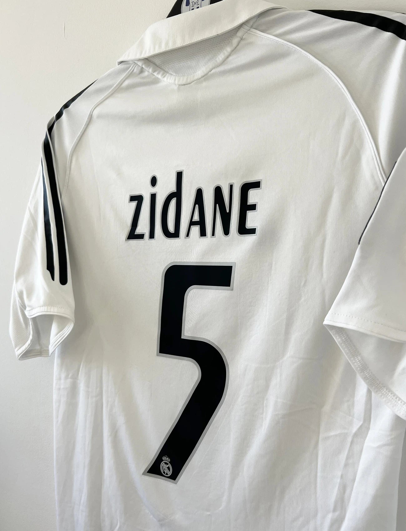 Maillot de foot vintage domicile du Real Madrid de la saison 2005/2006. Le maillot est de couleur blanc et noir. On peut retrouver l'équipementier adidas et le sponsor siemens. Le maillot est floqué du numéro 5 Zinedine Zidane. Le maillot possède l'étiquette d'authenticité avec les numéros 109879. Il s'agit d'un maillot authentique d'époque.