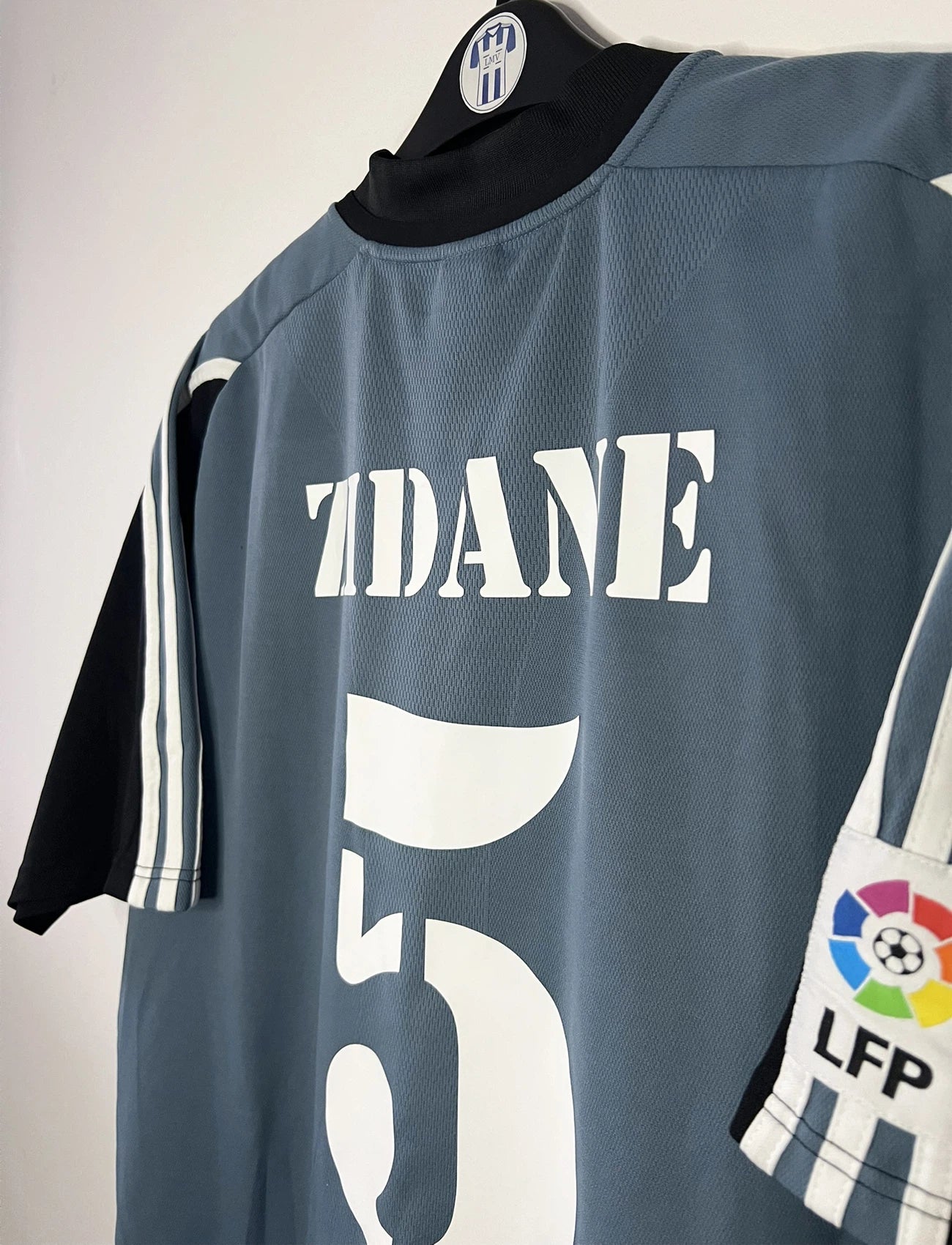Maillot de foot vintage third gris du real madrid de la saison 2001-2002. On peut retrouver l'équipementier Adidas et le sponsor RealMadrid.com. Le maillot est floqué du numéro 5 Zinedine Zidane. Il s'agit d'un maillot authentique d'époque.