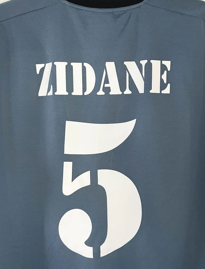 Maillot de foot vintage third gris du real madrid de la saison 2001-2002. On peut retrouver l'équipementier Adidas et le sponsor RealMadrid.com. Le maillot est floqué du numéro 5 Zinedine Zidane. Il s'agit d'un maillot authentique d'époque.