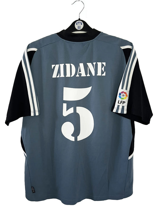 Maillot de foot vintage third gris du real madrid de la saison 2001-2002. On peut retrouver l'équipementier Adidas et le sponsor RealMadrid.com. Le maillot est floqué du numéro 5 Zinedine Zidane. Il s'agit d'un maillot authentique d'époque.