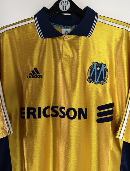 Maillot de foot vintage third doré de l'OM de la saison 1998/1999. On peut retrouver l'équipementier Adidas et le sponsor Ericsson. Il s'agit d'un maillot authentique d'époque.