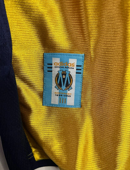 Maillot de foot vintage third doré de l'OM de la saison 1998/1999. On peut retrouver l'équipementier Adidas et le sponsor Ericsson. Il s'agit d'un maillot authentique d'époque.