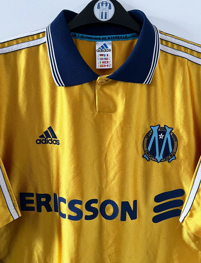 Maillot + short vintage third doré de l'OM 1998-1999. On peut retrouver l'équipementier Adidas et le sponsor Ericsson. Il s'agit d'un maillot et d'un short authentique d'époque.