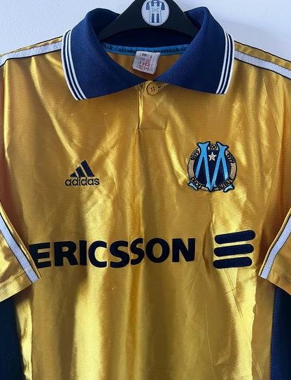 Maillot de foot vintage third doré de l'om 1998/1999. On peut retrouver l'équipementier Adidas et le sponsor Ericsson. Il s'agit d'un maillot authentique d'époque.