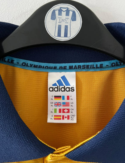 Maillot + short vintage third doré de l'OM 1998-1999. On peut retrouver l'équipementier Adidas et le sponsor Ericsson. Il s'agit d'un maillot et d'un short authentique d'époque.