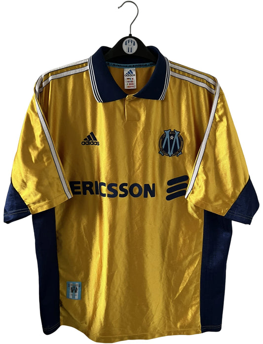 Maillot + short vintage third doré de l'OM 1998-1999. On peut retrouver l'équipementier Adidas et le sponsor Ericsson. Il s'agit d'un maillot et d'un short authentique d'époque.