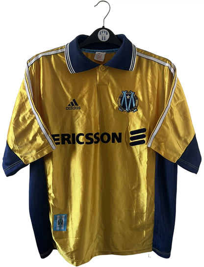Maillot de foot vintage third doré de l'om 1998/1999. On peut retrouver l'équipementier Adidas et le sponsor Ericsson. Il s'agit d'un maillot authentique d'époque.