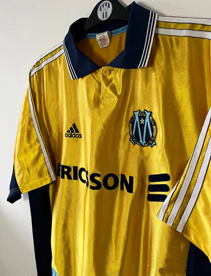 Maillot de foot vintage third doré de l'om 1998/1999. On peut retrouver l'équipementier Adidas et le sponsor Ericsson. Il s'agit d'un maillot authentique d'époque.