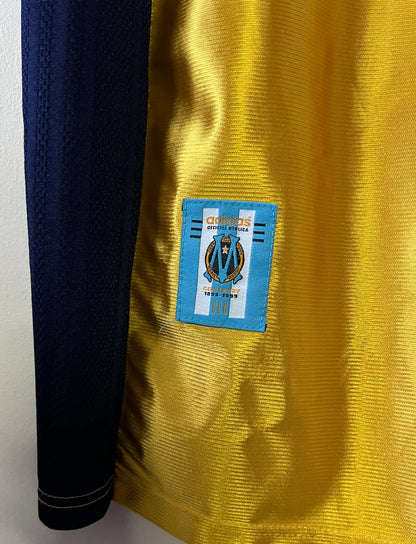 Maillot de foot vintage third doré de l'om 1998/1999. On peut retrouver l'équipementier Adidas et le sponsor Ericsson. Il s'agit d'un maillot authentique d'époque.