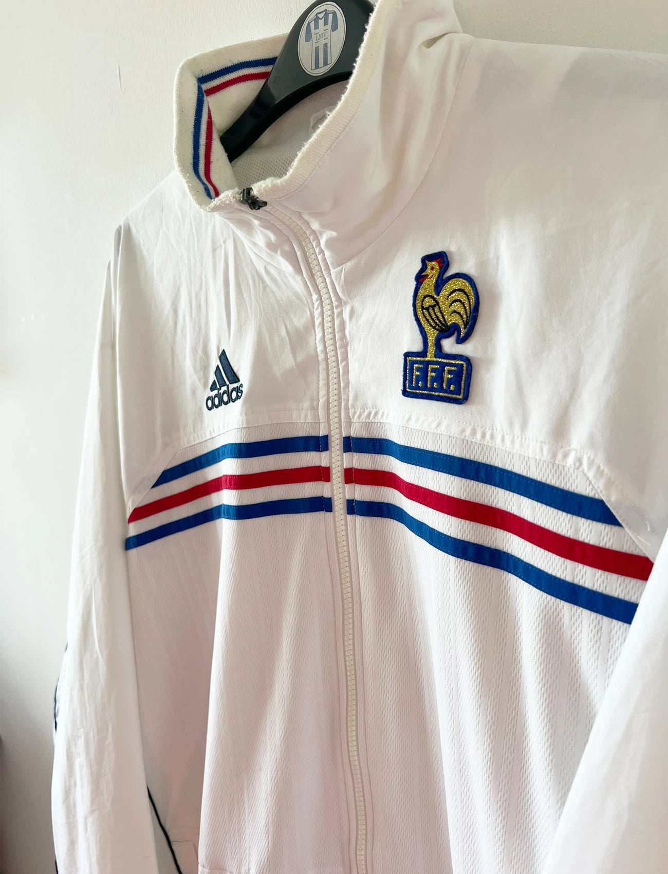 Veste de foot vintage blanche de l'Equipe de France 1998. On peut retrouver l'équipementier Adidas. Il s'agit d'une veste authentique d'époque.