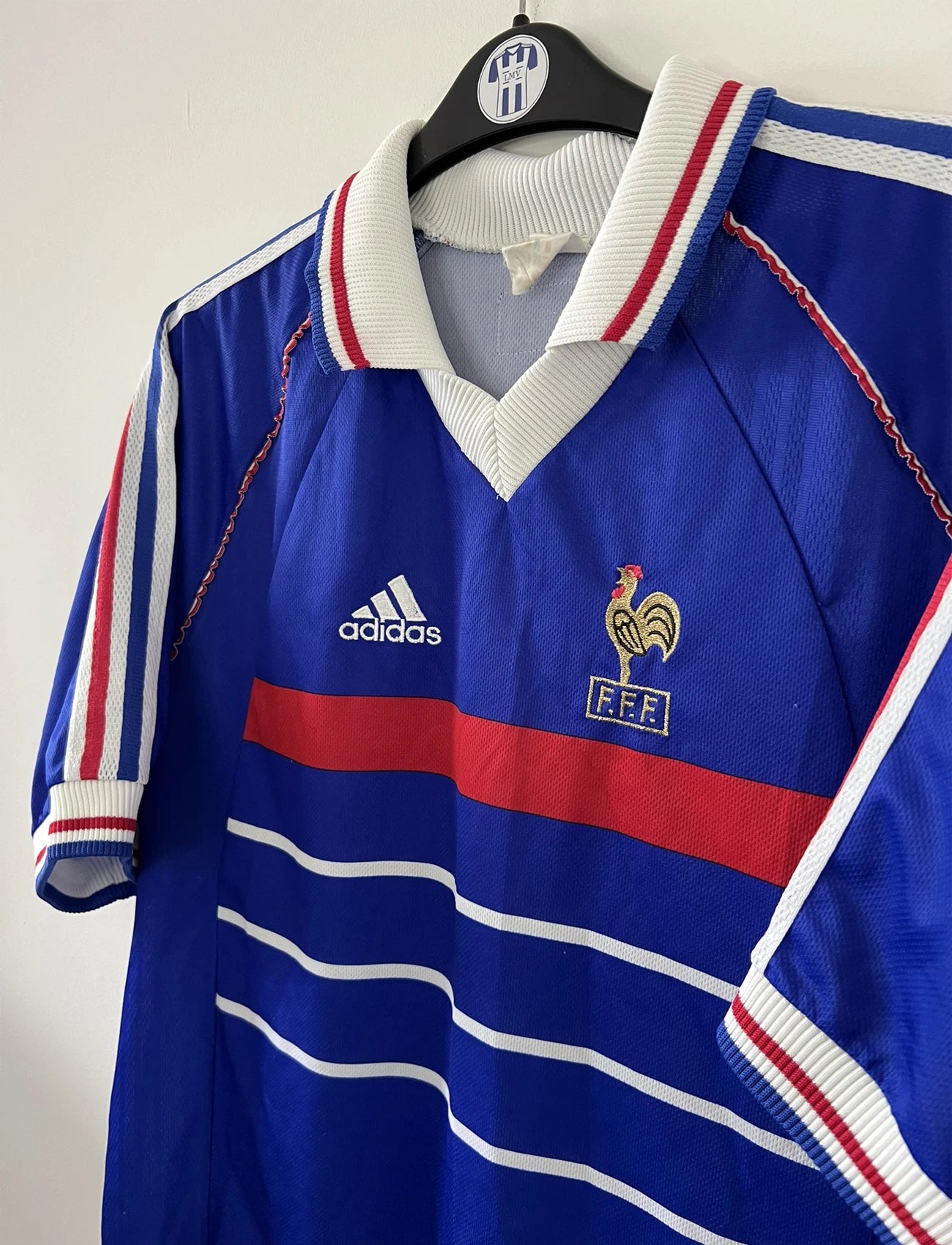 Maillot de foot vintage bleu, blanc et rouge de l'équipe de france 1998. On peut retrouver l'équipementier adidas. Il s'agit d'un maillot authentique édité avant la finale de la coupe du monde car celui-ci ne possède pas l'étoile.