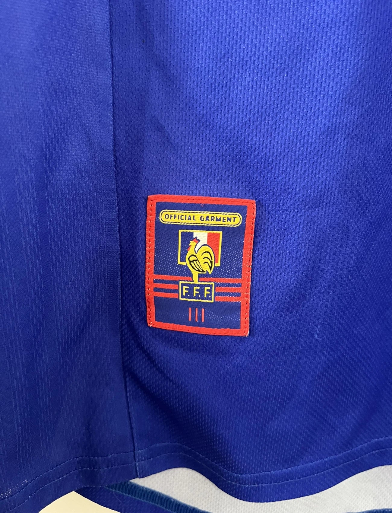 Maillot de foot vintage bleu, blanc et rouge de l'équipe de france 1998. On peut retrouver l'équipementier adidas. Il s'agit d'un maillot authentique édité avant la finale de la coupe du monde car celui-ci ne possède pas l'étoile.