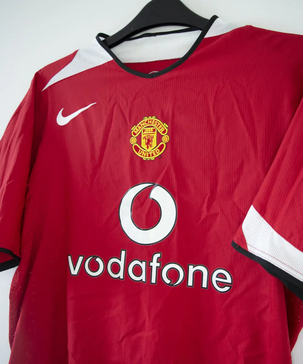 Maillot domicile de manchester united rouge, blanc et noir, édité lors de la saison 2004-2005 et la saison 2005-2006. On peut retrouver l'équipementier nike et le sponsor vodafone.