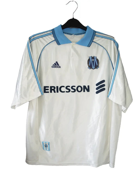Maillot domicile de l'om de la saison 1998-1999. Le maillot est de couleur blanc et bleu. On peut retrouver l'équipementier adidas et le sponsor ericsson