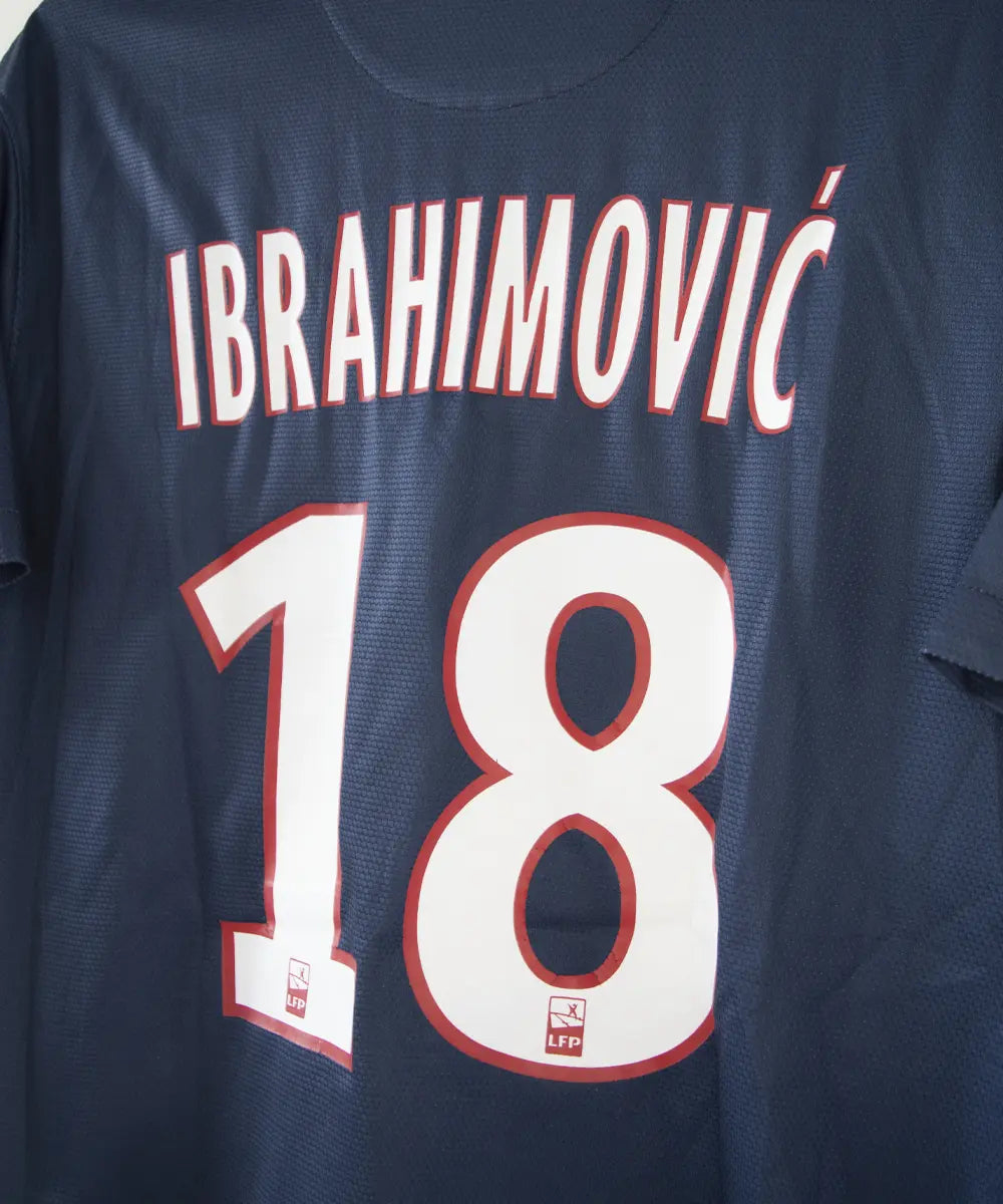 Maillot domicile du PSG bleu blanc et rouge, de la saison 2012-2013. On peut retrouver l'équipementier nike et le sponsor fly emirates. Le maillot est floqué du numero 18 Zlatan Ibrahimovic. Sur cette photo on peut voir le flocage de côté