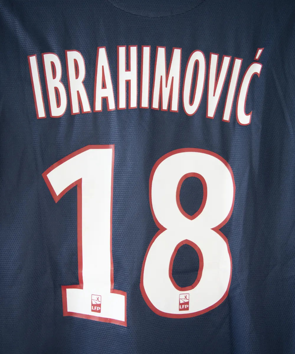 Maillot domicile du PSG bleu blanc et rouge, de la saison 2012-2013. On peut retrouver l'équipementier nike et le sponsor fly emirates. Le maillot est floqué du numero 18 Zlatan Ibrahimovic. Sur cette photo on peut voir le flocage de près