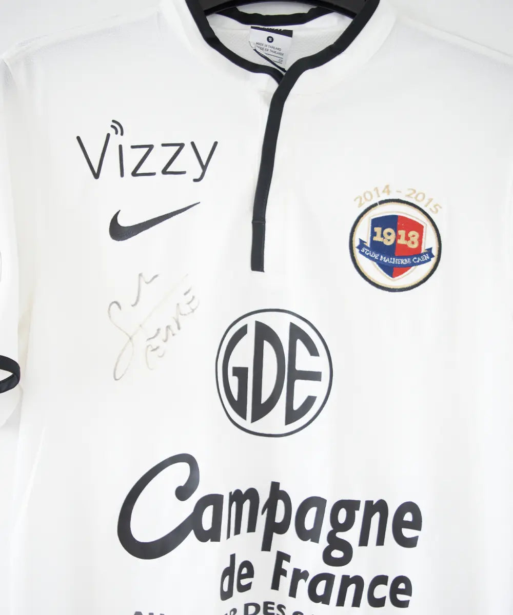 Maillot third du SM Caen de la saison 2014-2015 de couleur blanc et noir. On peut retrouver l'équipementier nike, le sponsor GDE et le sponsor SAS Malus. Le maillot est floqué du numéro 2 Nicolas Seube. Le maillot est aussi signé par Seube