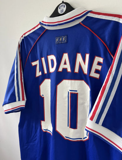 Maillot de foot vintage domicile de l'équipe de france 1998. On peut retrouver l'équipementier adidas. Le maillot est de couleur bleu blanc et rouge. Le maillot est floqué du numéro 10 Zinedine Zidane. Il s'agit d'un maillot authentique d'époque.
