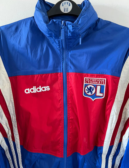 Veste de foot vintage bleu de l'OL 1996. On peut retrouver l'équipementier Adidas. Il s'agit d'une veste authentique d'époque.