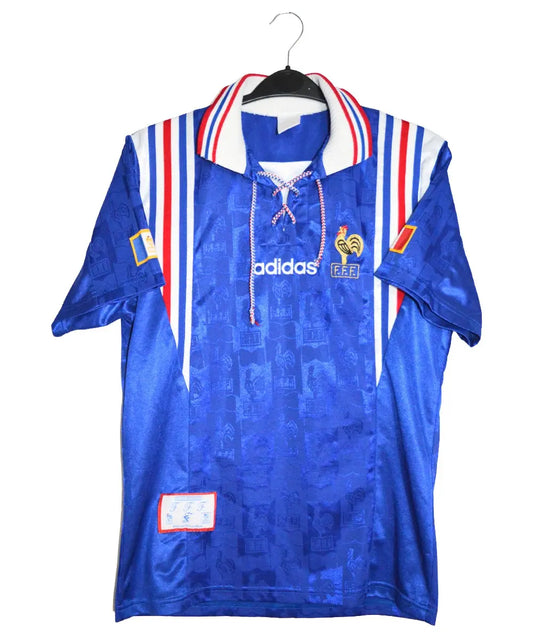Maillot de foot retro authentique de l'équipe de france 1996. Le maillot est au couleur de la france (bleu, blanc, rouge). Des motifs de coqs sont brodés dans le maillot. On retrouve aussi l'équipementier adidas