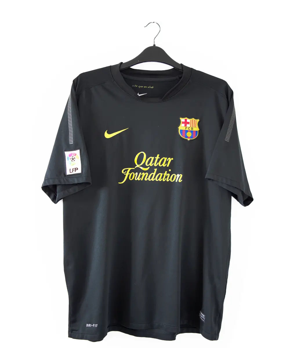 Maillot extérieur du FC Barcelone lors de la saison 2011-2012. Le maillot est de couleur noir et jaune. On peut retrouver l'équipementier nike, le sponsor qatar foundation et unicef. Le maillot est floqué du numéro 8 iniesta
